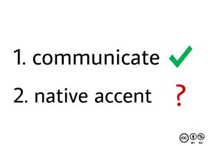 An illustration showing the word 'Communicate' with a checkmark and 'Native Accent' with a question mark in front of it, emphasizing the importance of focusing on communication in language learning process.