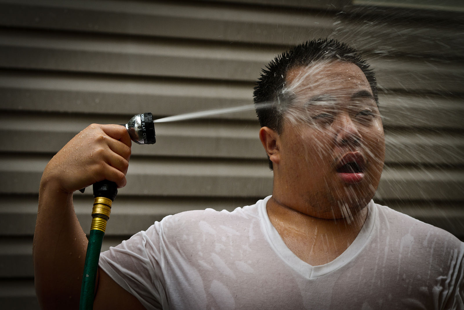 Man spraying himself in the face with a hose.