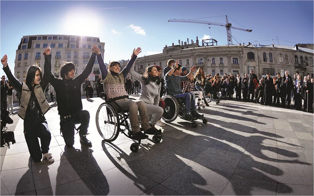 Line of adults in wheelchairs and adults kneeling raise hands triumphantly.