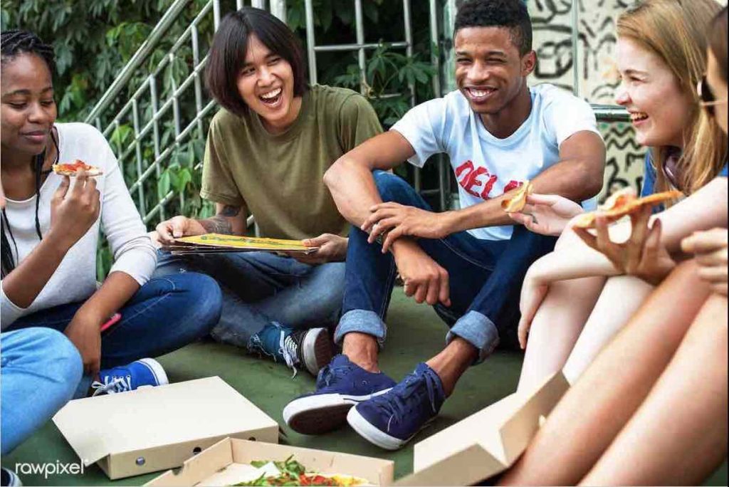 diverse group of teens laugh and eat pizza.