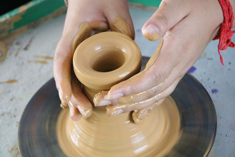 Image of two hands sculpting wet clay at a potter's wheel.