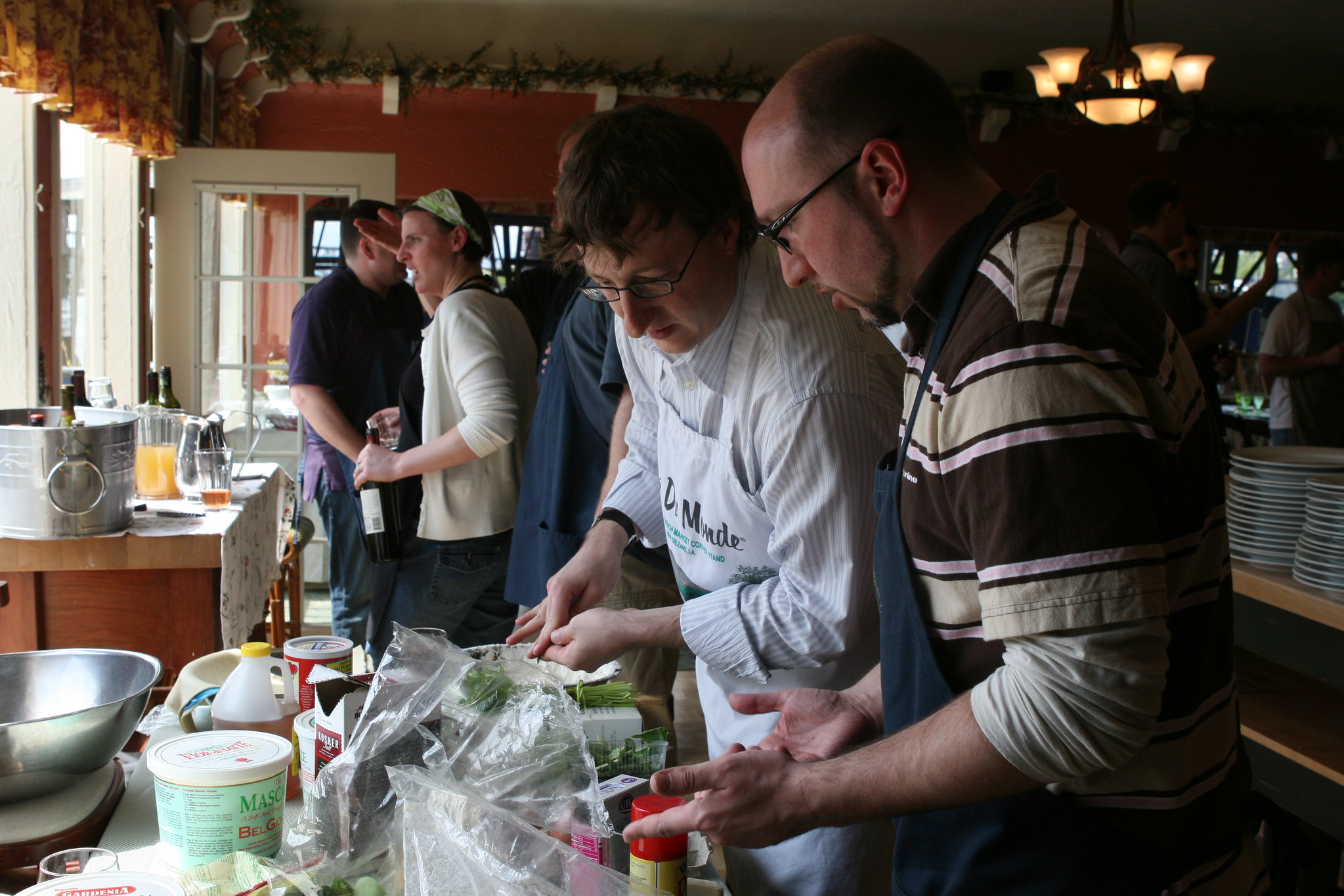 In a crowded kitchen two cooks stand over a counter counter full of ingredients.
